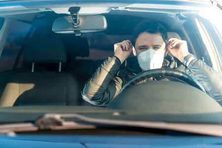 man puts medical mask on face in car. prevention against coronavirus covid-19. quarantine at the time of the viral epidemicの写真素材