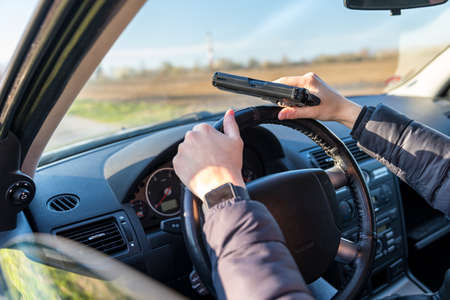 young man with gun in hand in passenger car on drivers seat
