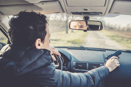 driver with gun in hand in passenger car on dirt road.の写真素材