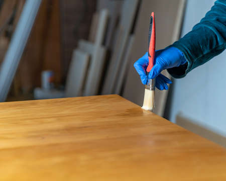 coating of wooden surface with protective varnish. hand in blue rubber glove uses brush.の写真素材