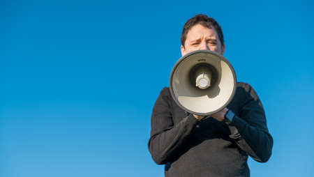 young man voices into a megaphone instructions for exercise. Copy spaceの写真素材