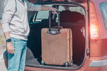 A young man puts luggage in the trunk of a car.の写真素材