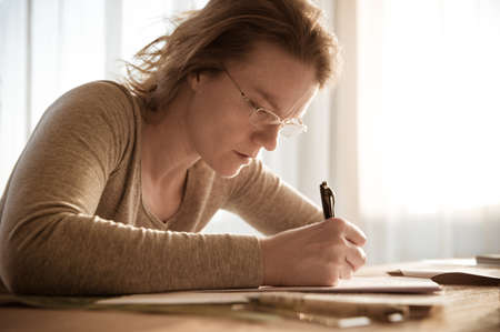 young woman focused on writing homework while studying at homeの写真素材