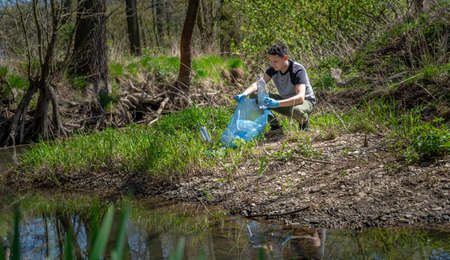 cleaning of plastic waste on the river bank by a volunteer. Helping nature and protecting the environmentの写真素材