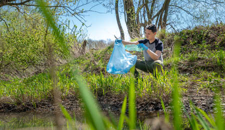 collecting garbage in a plastic bag, a volunteer man helps in the forest on the river bank