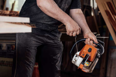 The man starts a hand-held chainsaw in a carpentry shopの写真素材