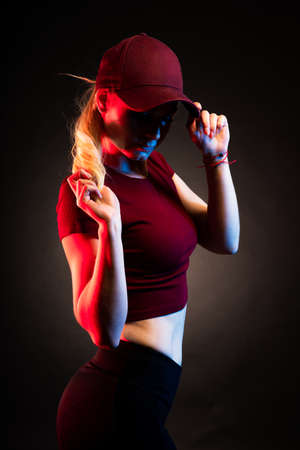 Portrait of a woman in a baseball cap on a black background. red and blue color illuminates the figureの写真素材