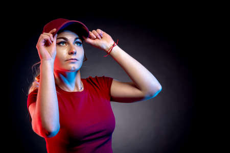 Portrait of a woman in a baseball cap on a black background. red and blue color illuminates the figureの写真素材