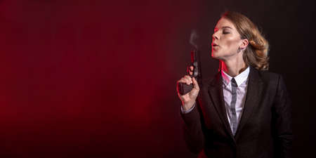 blowing smoke out of a gun after a shot. portret of a business woman on a dark background. banner...