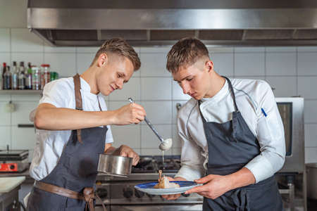 preparing meat with sauce by two young chefsの写真素材