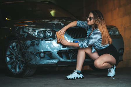 A young attractive woman washes a car with a sponge and foam