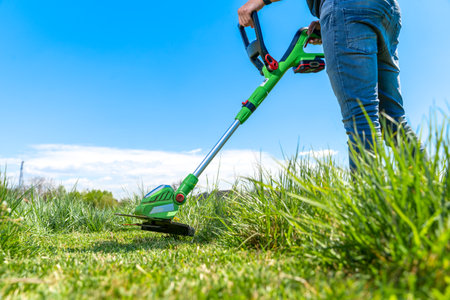 man mows the grass in the meadow with a hand-held cordless lawnmowerの写真素材