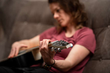 woman playing guitar at home on the couchの写真素材