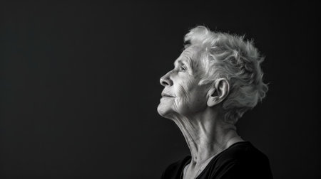 Senior woman looking up with hope on dark backgroundの素材