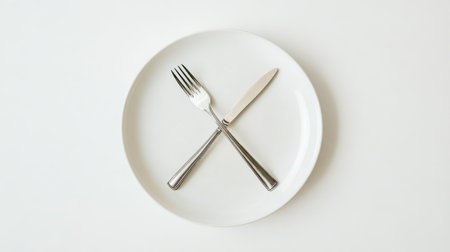 Empty plate with knife and fork making a cross over white backgroundの素材