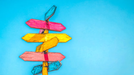 Colorful wooden signpost pointing in different directions against blue skyの素材