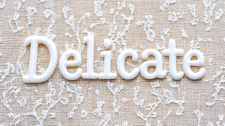 Delicate white letters spelling delicate resting on beige laceの素材