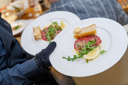 Waiter serving beef carpaccio appetizers with arugula and lemon