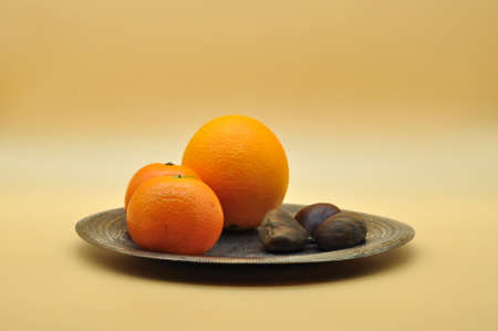 Still life of oranges and tangerines resting on an elegant and antique silver plate on a neutral orange backgroundの写真素材
