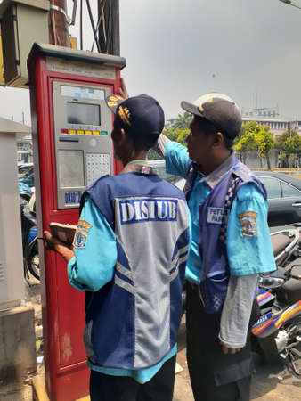 Jakarta, Indonesia - October 3, 2019: Traffic warden and parking attendant checking a parking meter.のeditorial素材