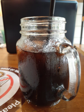 A jar with cold black cofee on wooden table.の写真素材