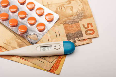 medicine tablet, thermometer indicating 38.9 degrees and Brazilian money billsの写真素材