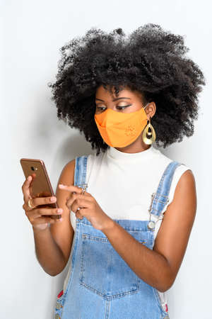 YOUNG WOMAN USING FACIAL PROTECTION MASK AND SENDING MESSAGE WITH MOBILEの写真素材