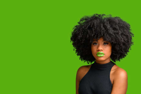 black girl with afro hair style looking at camera, photographed over green background.の写真素材