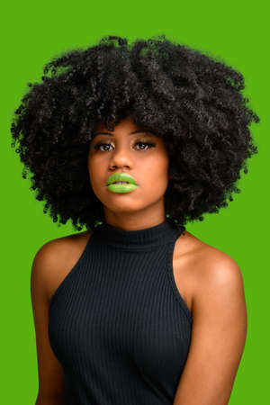 black girl with afro hair style looking at camera, photographed over green background.の写真素材