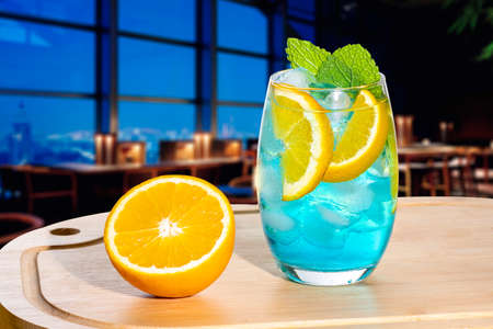 a blue cocktail glass on a wooden board, decorated with orange, mint, and a picture of a bar in the...