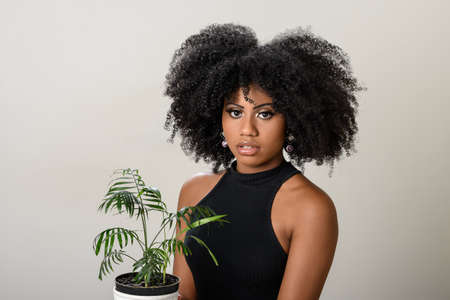 black woman holding a vase with a small plant, palm tree, isolated on gray backgroundの写真素材
