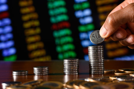 Man's hand putting coin to stack of coins on the table with stock market chart backgroundの写真素材