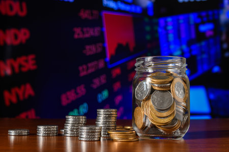 glass jar with coins, stack of coins in front of a financial market chartの写真素材