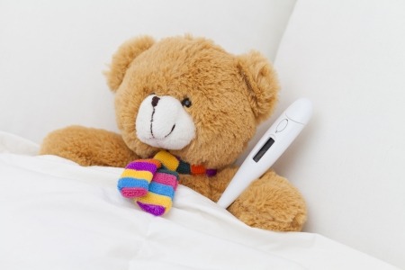 Teddy bear taking cold temperature in bedの写真素材