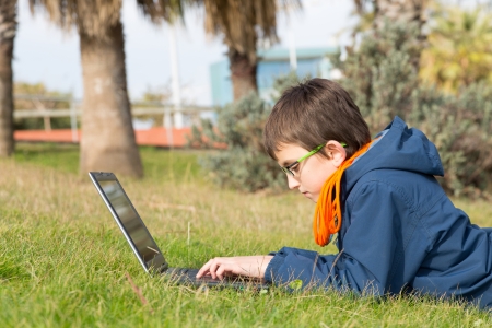 Boy with a laptop lying on the grass in a parkの写真素材
