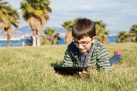 Boy with a laptop lying on the grass in a parkの写真素材