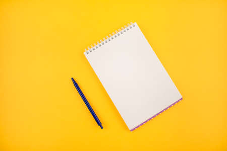 Notepad with a white sheet on a yellow background. Man's hand tries to write.の写真素材