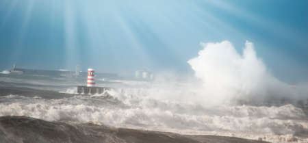 lighthouse on the breakwater and broken waveの写真素材