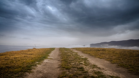 Dirt road in the foggy mountains and stormy sky.の写真素材