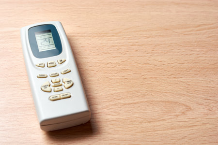 Air conditioner remote set at 24 degrees celsius on wooden desk. Concept of energy saving and...