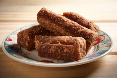 Panela slices in a small plate on wooden table. Also known as rapadura, it is unrefined whole cane sugar typical of Central and Latin America.の写真素材