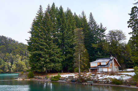 NEUQUEN, ARGENTINA - SEPTEMBER 8, 2015: Small rustic cabin surrounded by tall green pine trees next to the pier of Mansa Bay in Villa La Angostura, NeuquÃ©n, Argentina. View of the Nahuel Huapi Lake.のeditorial素材