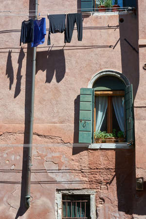 Details of old cracked wall, window and hanging laundry of traditional house next to water canal in Venice, Italy.の写真素材
