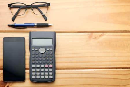 Top view of home office rustic wooden work table with calculator, pen, mobile phone and glasses. Space for text and graphics on the right side.の写真素材