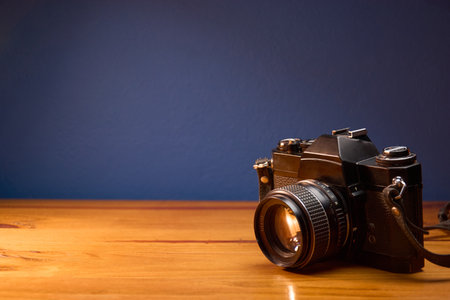 Horizontal front view of old analog camera on wooden desk against blue wall. Professional photography camera. Copyspace.の写真素材
