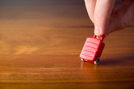 Male hand carrying miniature toy suitcase. Concept of travel, passenger with luggage. Travel insurance, booking and planning.の写真素材