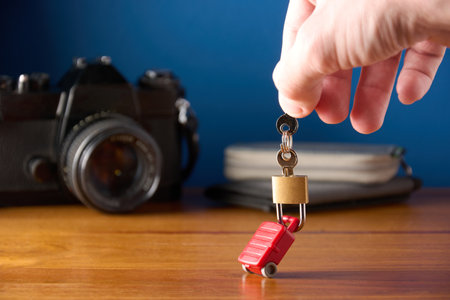 Male hand holding keys and padlock locked on miniature toy suitcase. Concept of travel insurance, safe travel. Blue background with copy space.の写真素材