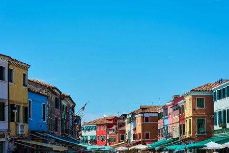 View of top part of buildings forming a line against blue cloudless sky on sunny spring day in Burano, Italy. Background with copy space.のeditorial素材