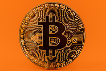 Gold bitcoin coin against vibrant orange backdrop.