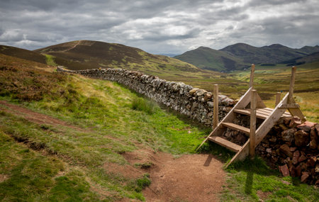 Stile with wooden steps over a stone wall on a trail in the pentland hills in Edinburgh. rural british landscapeの写真素材